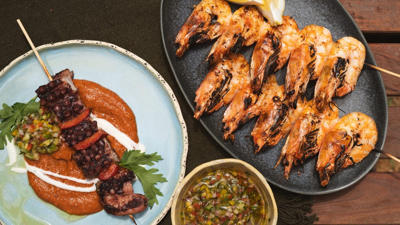 Gambas e espeto de carne grelhados na brasa, servidos com molho romesco e chimichurri