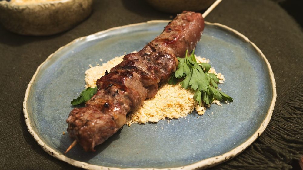 Espeto de picanha grelhada num prato azul com farofa e ervas